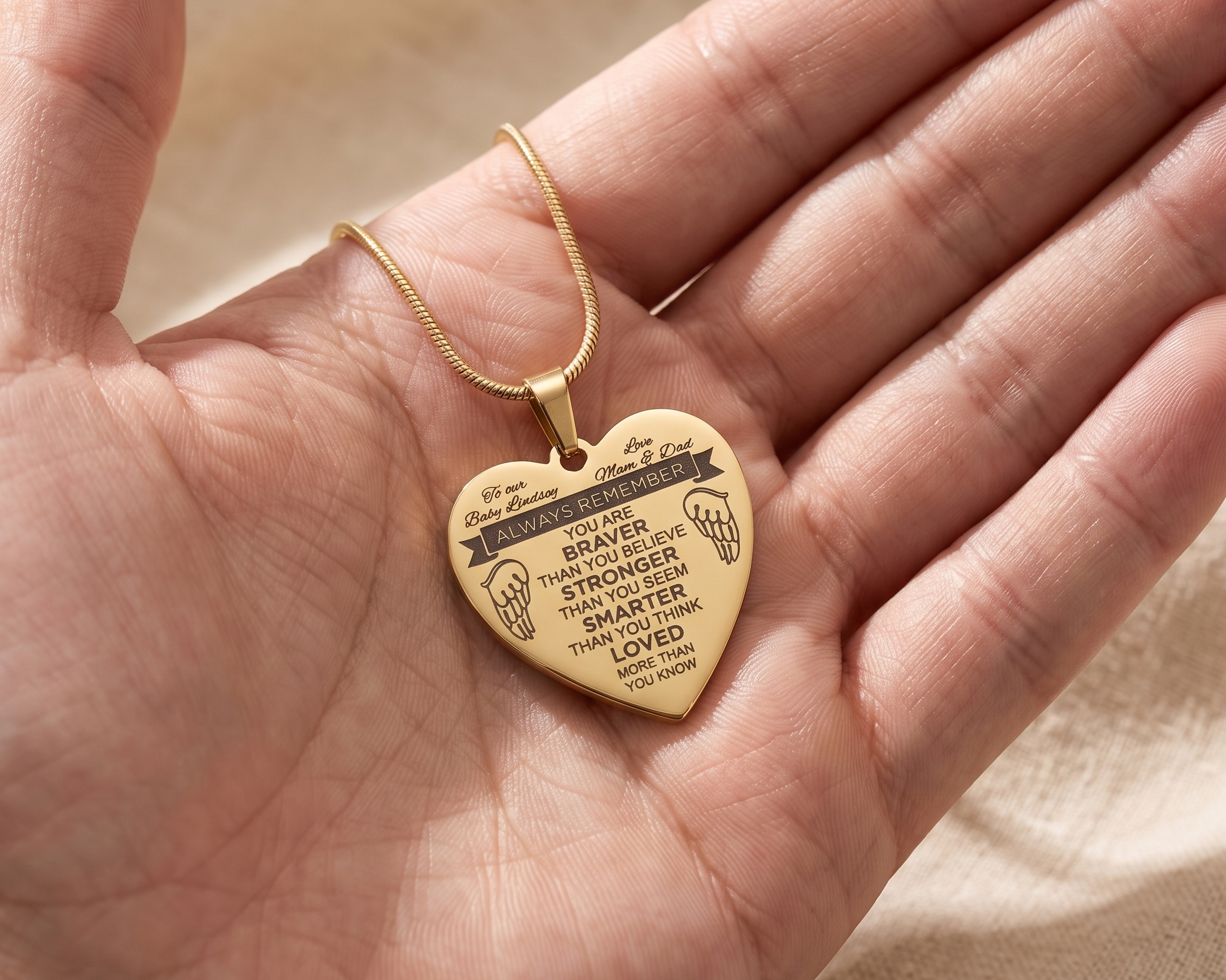 A woman's hand resting on an engraved name pendant at her collarbone in soft morning light
