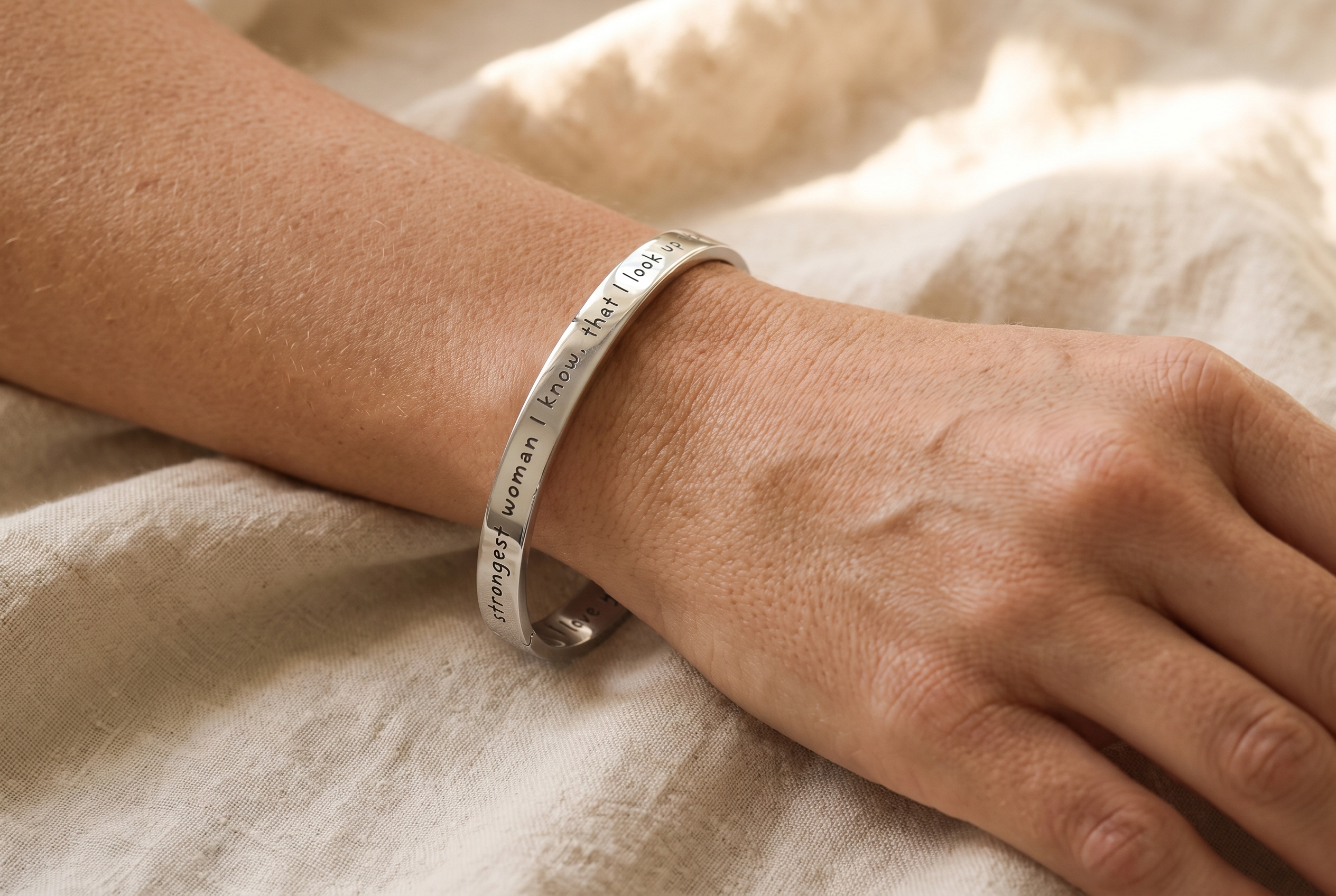Woman's wrist wearing an engraved silver Promise Bangle with a short name, resting on a linen sleeve