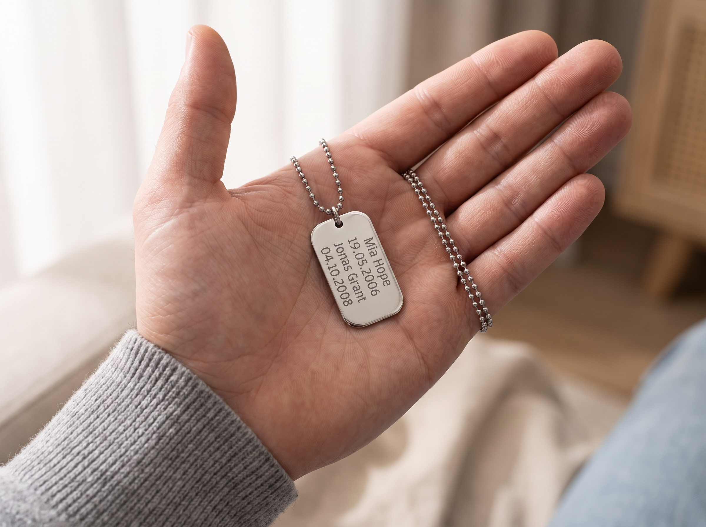 A dad's hand holding a personalised silver dog tag engraved with his children's names