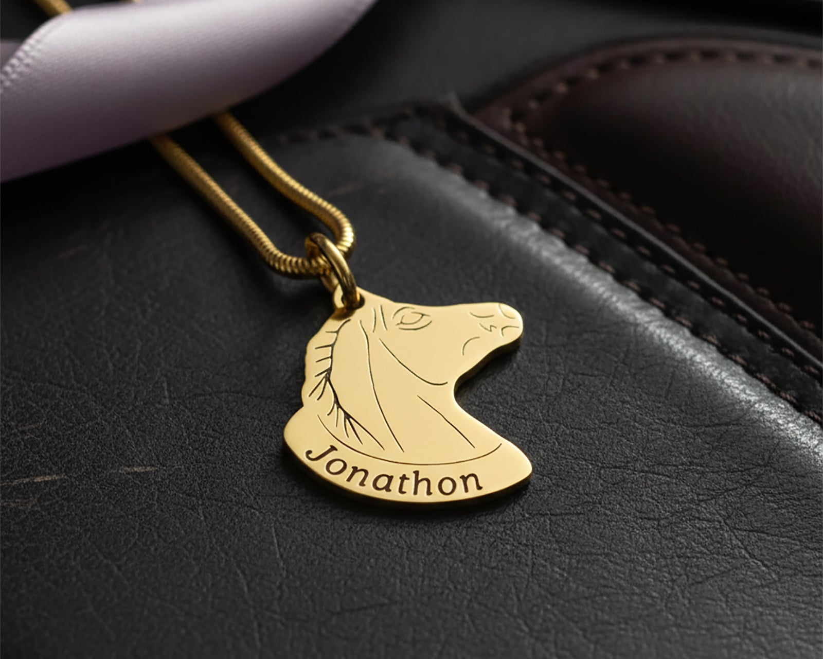 Belle Fever Horse Head Necklace with Custom Name in gold resting on black leather background, custom engraved horse pendant necklace, luxury personalised equestrian jewellery gift.