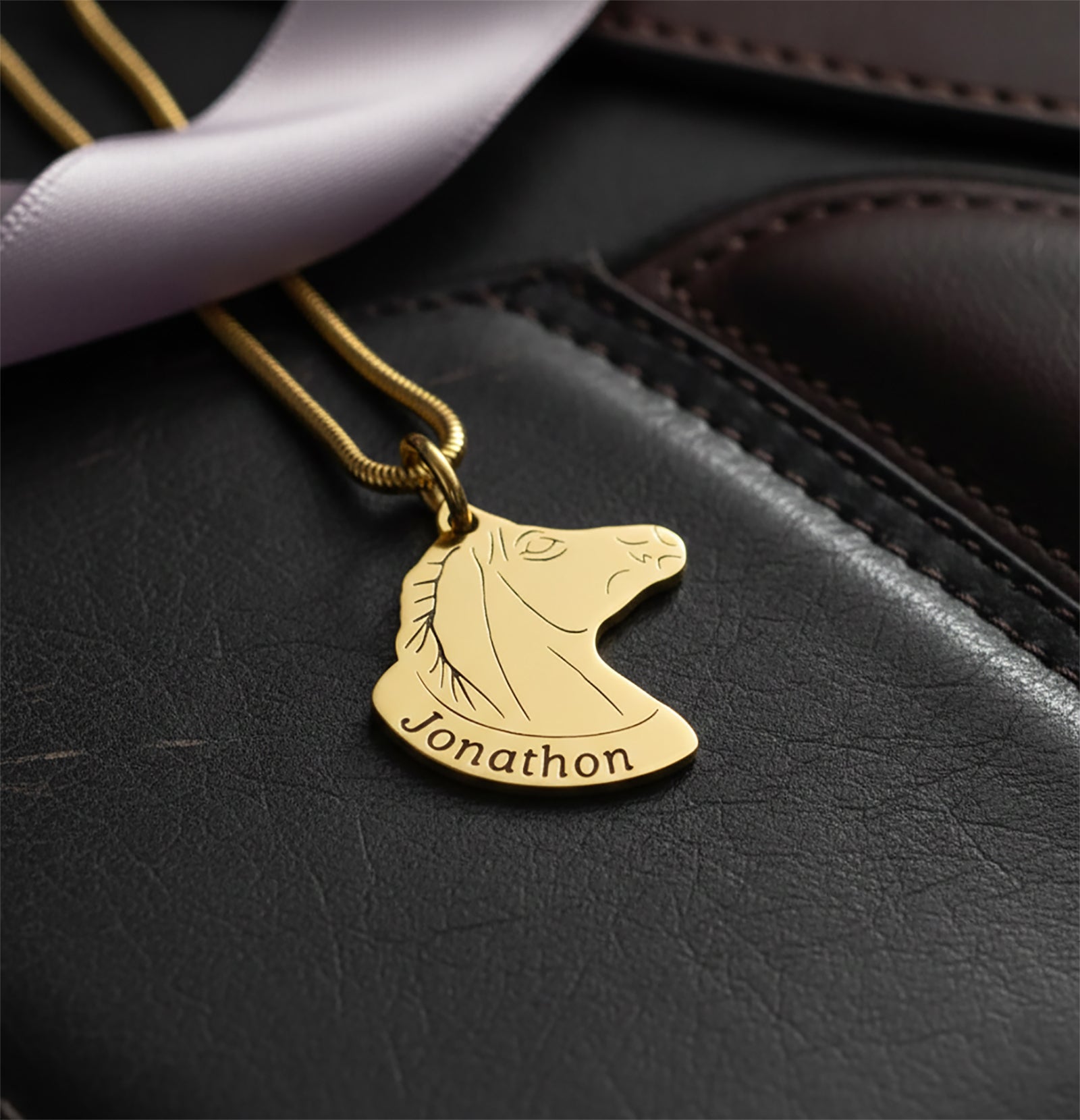 Belle Fever Horse Head Necklace with Custom Name in gold resting on black leather background, custom engraved horse pendant necklace, luxury personalised equestrian jewellery gift.
