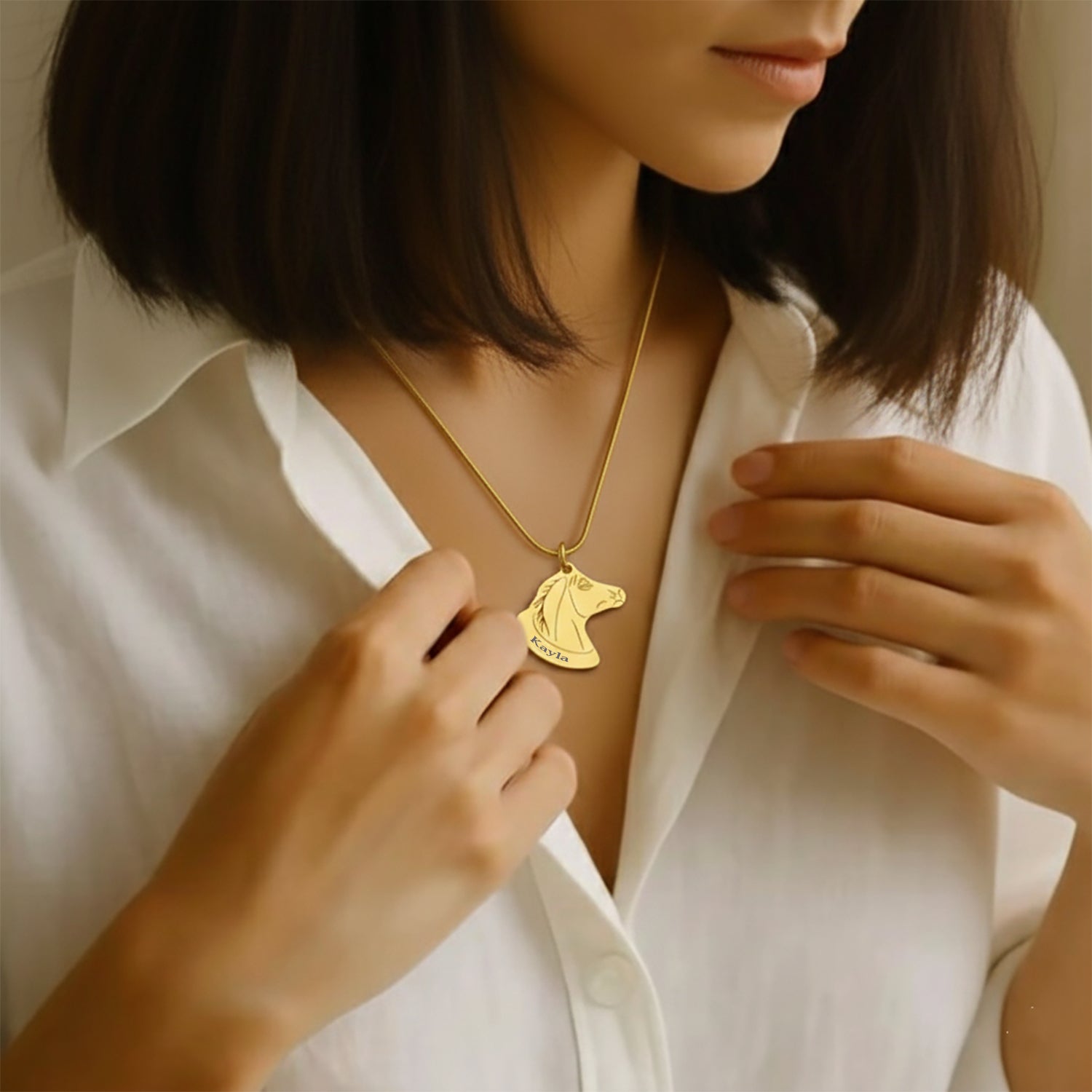 Belle Fever Horse Head Necklace with Custom Name worn by woman in white blouse, gold personalised horse pendant necklace for equestrian lovers, custom engraved name jewellery gift.
