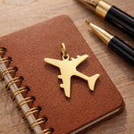 Belle Fever gold plane charm for keyring on brown agenda, travel airplane charm gift, elegant 3D metal detail.