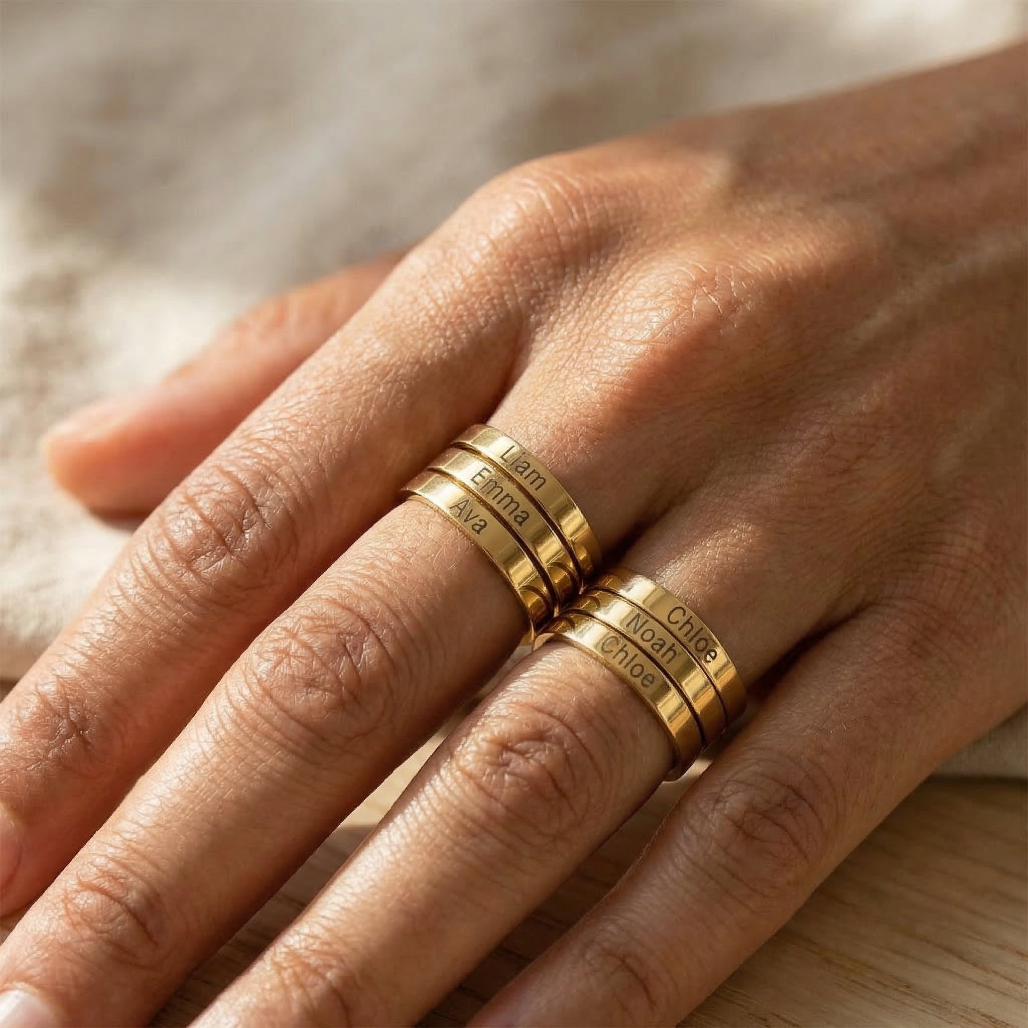 Hand wearing gold rings with engraved text on a neutral background
