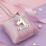 Unicorn head necklace with birthstone and custom engraved name in silver finish on pink background.
