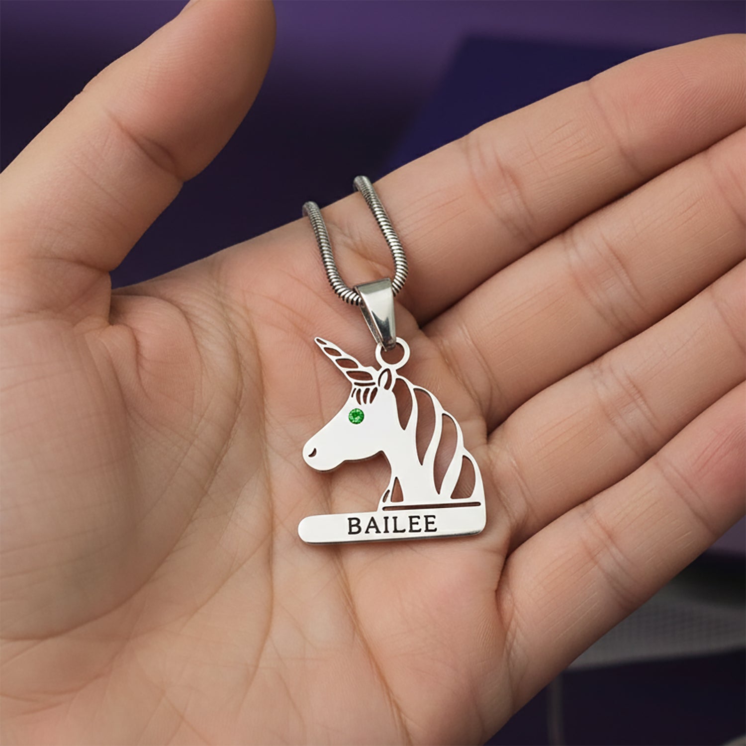 Personalized unicorn head necklace with birthstone and name engraving held in hand.