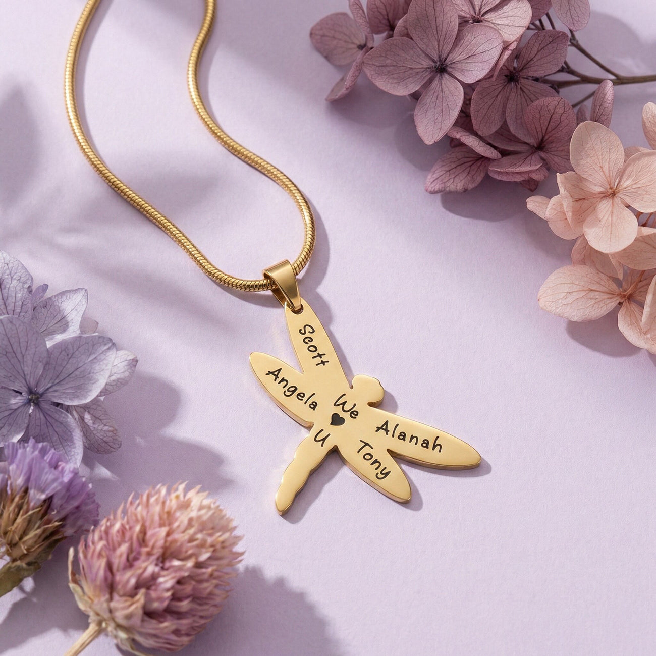 Belle Fever Dragonfly Necklace with Custom Engraved Names in polished gold on soft lavender background with floral accents, symbol of strength and transformation jewellery gift.
