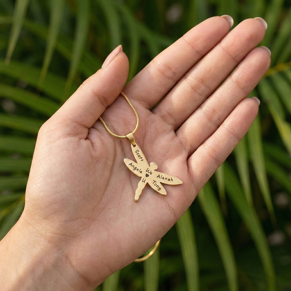 Belle Fever Dragonfly Necklace with Custom Engraved Names resting on palm against green leaves, nature inspired strength and transformation jewellery gift.