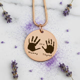 Belle Fever Hand on My Heart Necklace — rose gold handprint pendant styled on fabric with delicate florals, a touching memorial keepsake for remembering loved ones.