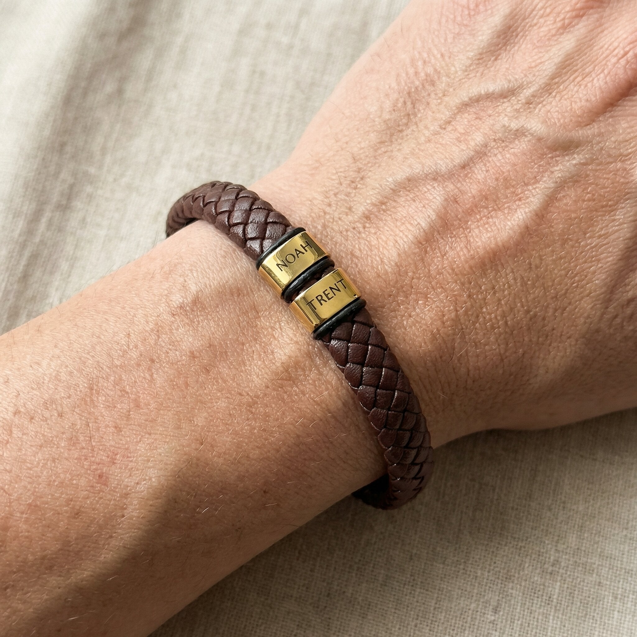 Man wearing personalised brown leather bracelet with engraved gold charms, custom design option